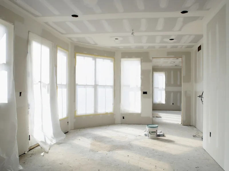 A bright bay-windowed room with its drywall taped and mudded, ready for finishing
