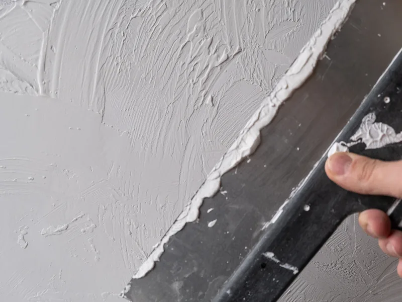 White drywall compound spread over a grey wall with the edge of a broad knife