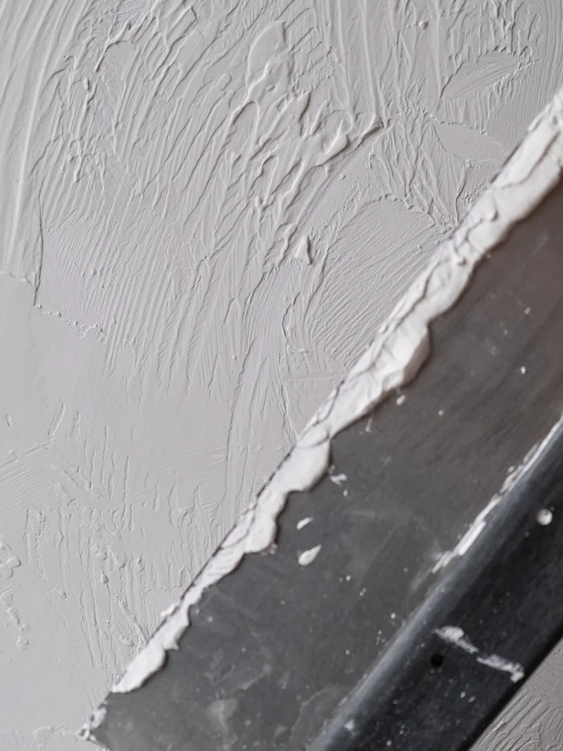 White compound spread over a grey wall with the edge of a broad knife
