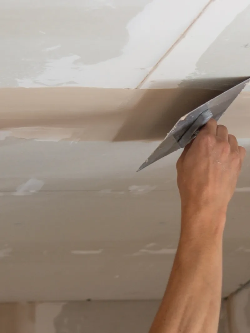 A trowel worked overhead along a new ceiling seam at arm’s length