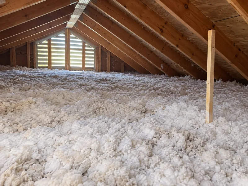 A deep, even bed of loose-fill insulation across an attic floor with a plain measuring stick pushed into it