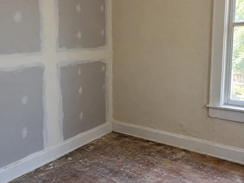 New taped drywall on one wall meeting an older, repeatedly painted wall in the same inside corner