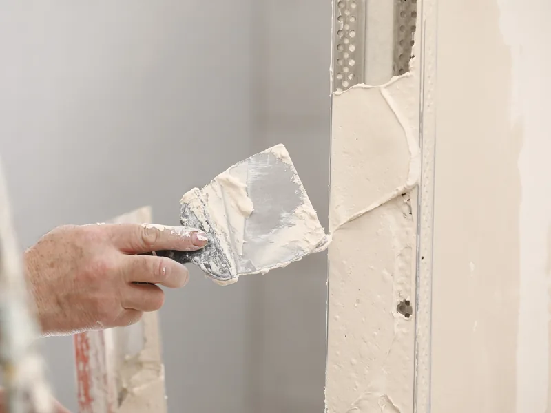 A trowel loaded with plaster pressed into a patch at the edge of a wall