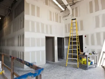 A tall commercial interior with boarded walls and a ladder against one of them
