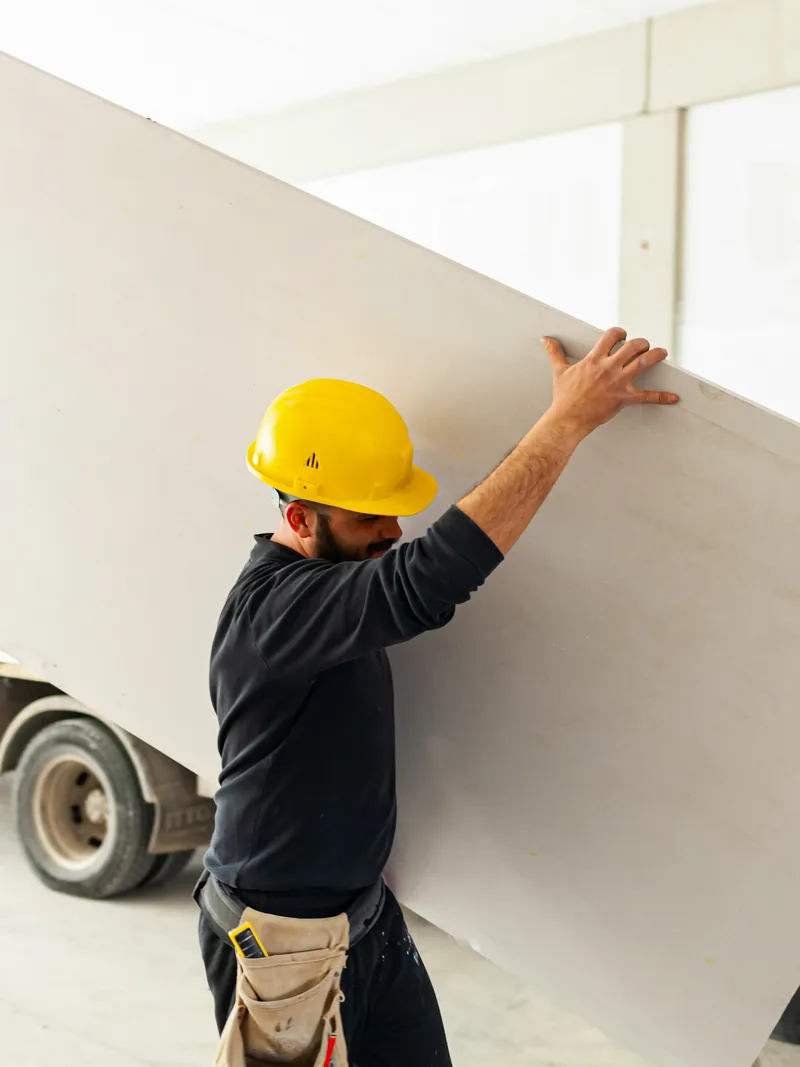A worker lifting a single board down from a flatbed truck as the drywall is stocked