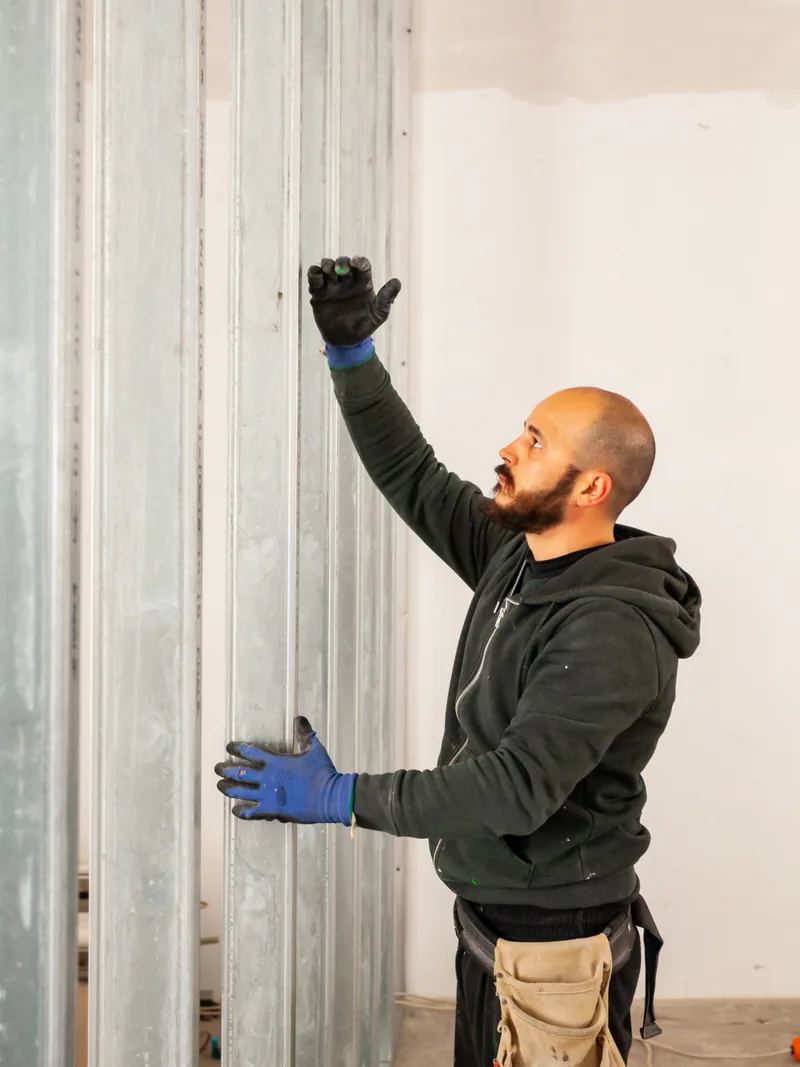 A worker setting a stud into the floor track as a partition wall is laid out