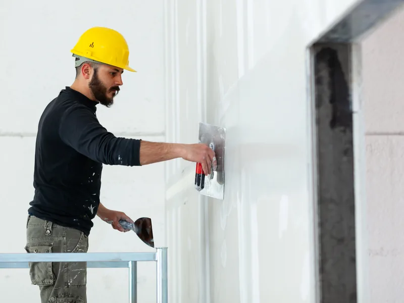 A worker finishing the face of a drywall wall next to a squared structural column