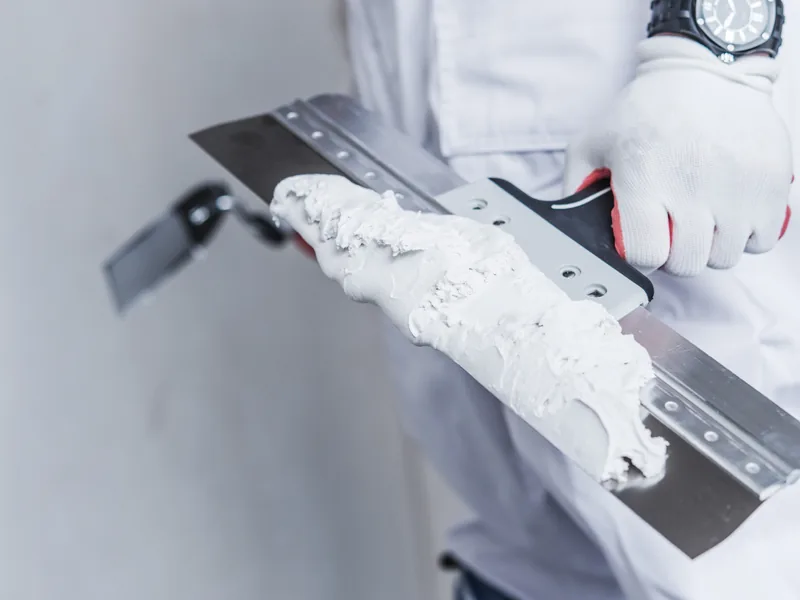 A broad drywall knife held up loaded with a ridge of joint compound