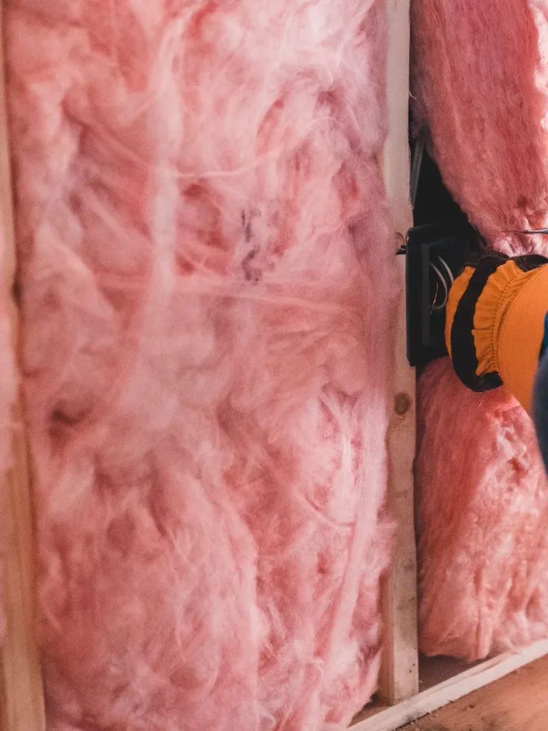 Fibreglass insulation batts pressed into a stud bay by a gloved hand