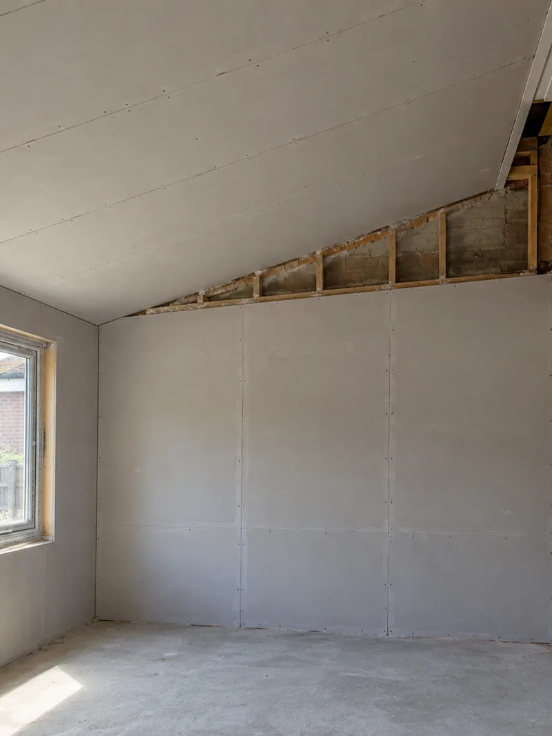 A converted carport boarded out with a new sloped ceiling against one wall of exposed brick