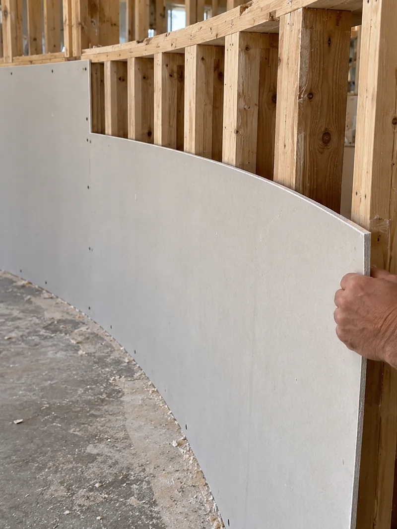 A flexible sheet of board bent around closely spaced studs on a tight arc, held in by hand at the free end