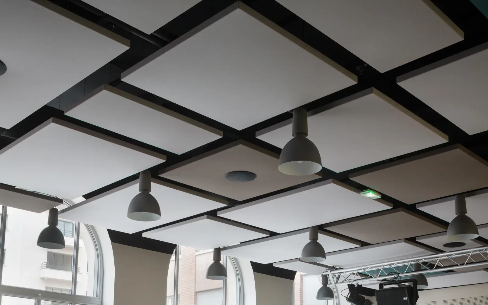 A black coffered acoustical ceiling grid with pendant lights over an open commercial floor