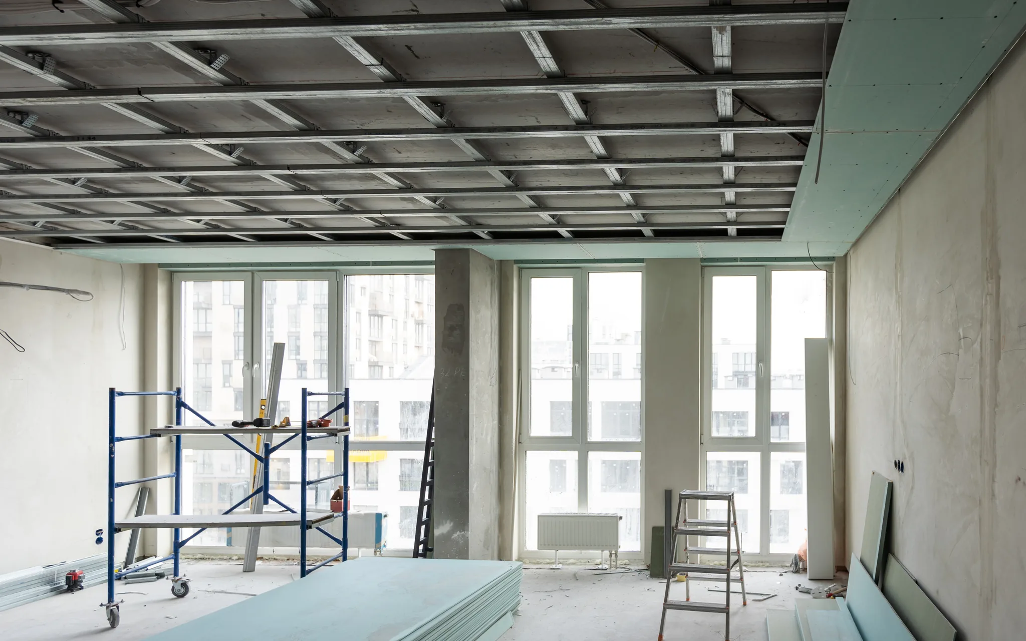 Commercial drywall work underway, a scaffold tower beneath an open suspended ceiling grid