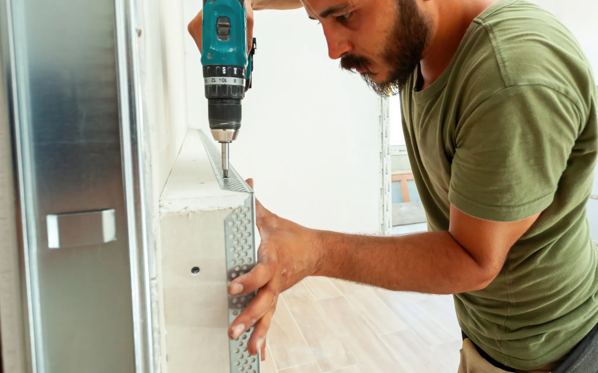 A worker installing a metal corner bead on an outside corner with a drill