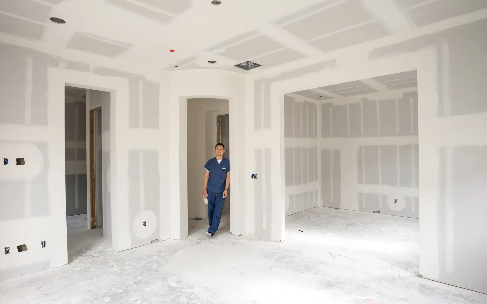 A long room boarded out in drywall with a single figure standing at the far end