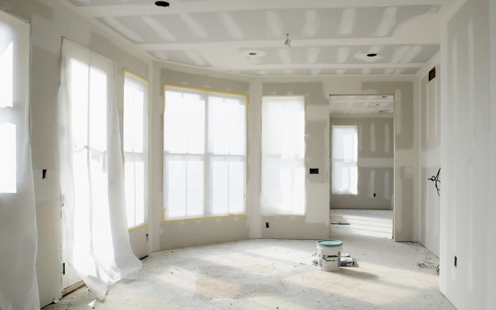 A bright bay-windowed room taped and mudded, ready for drywall finishing and texture