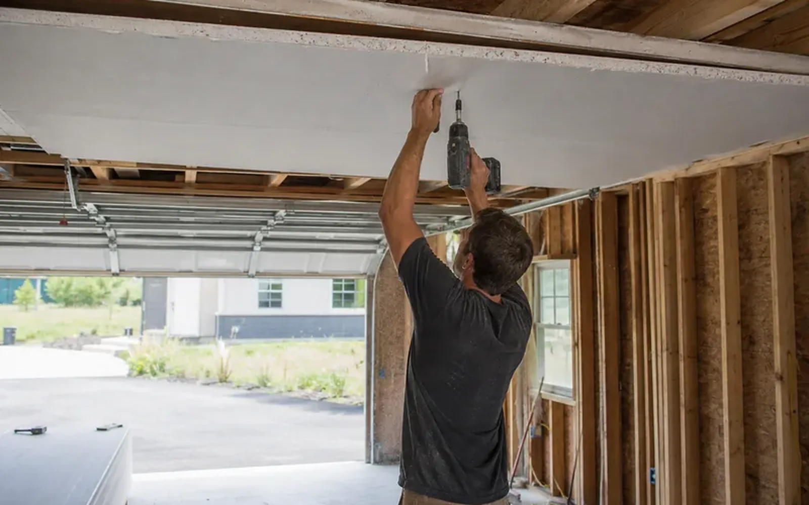 A worker screwing fire-rated board to the ceiling of an open garage