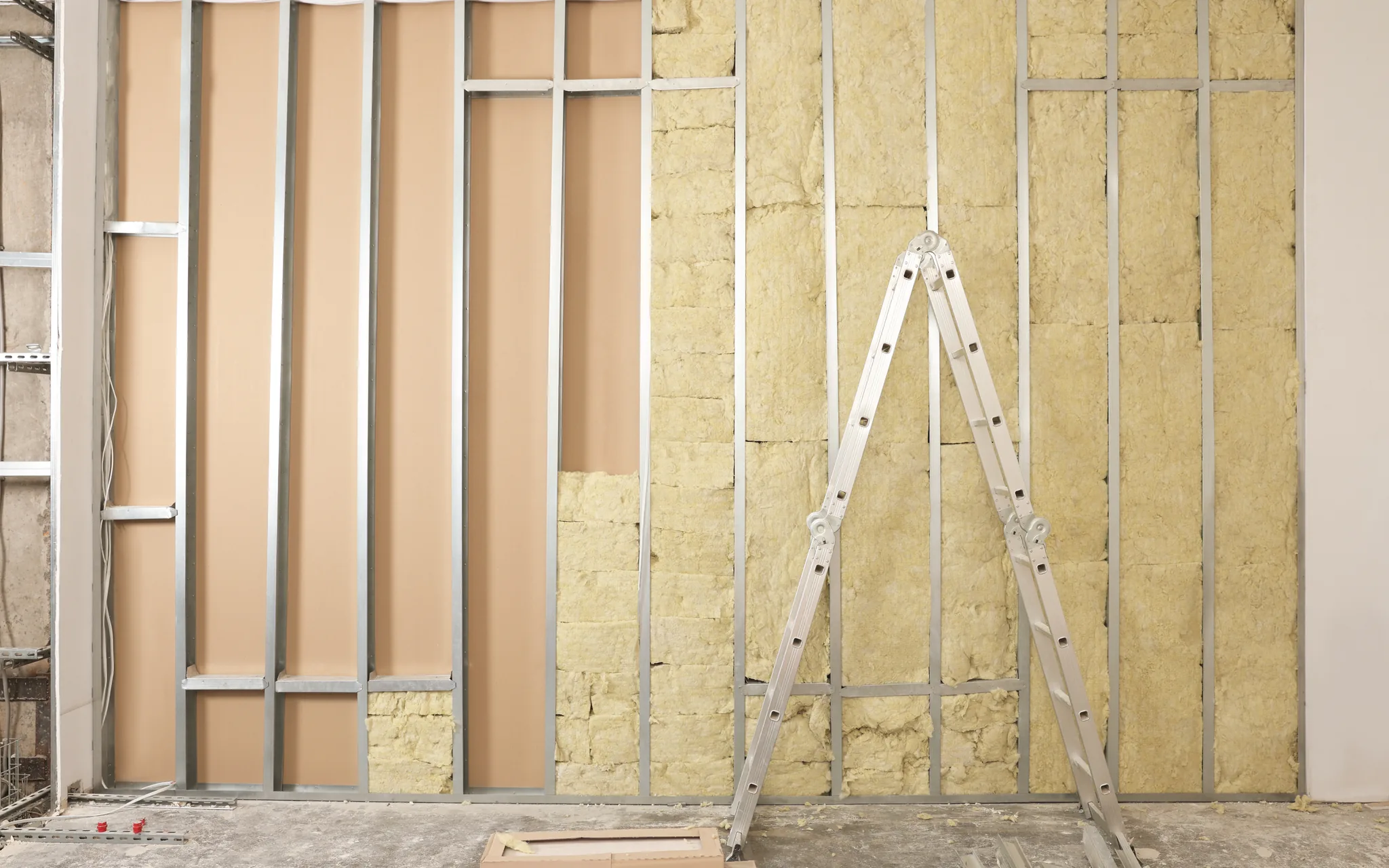 A framed wall filled with insulation batts before the drywall goes on, a stepladder in front