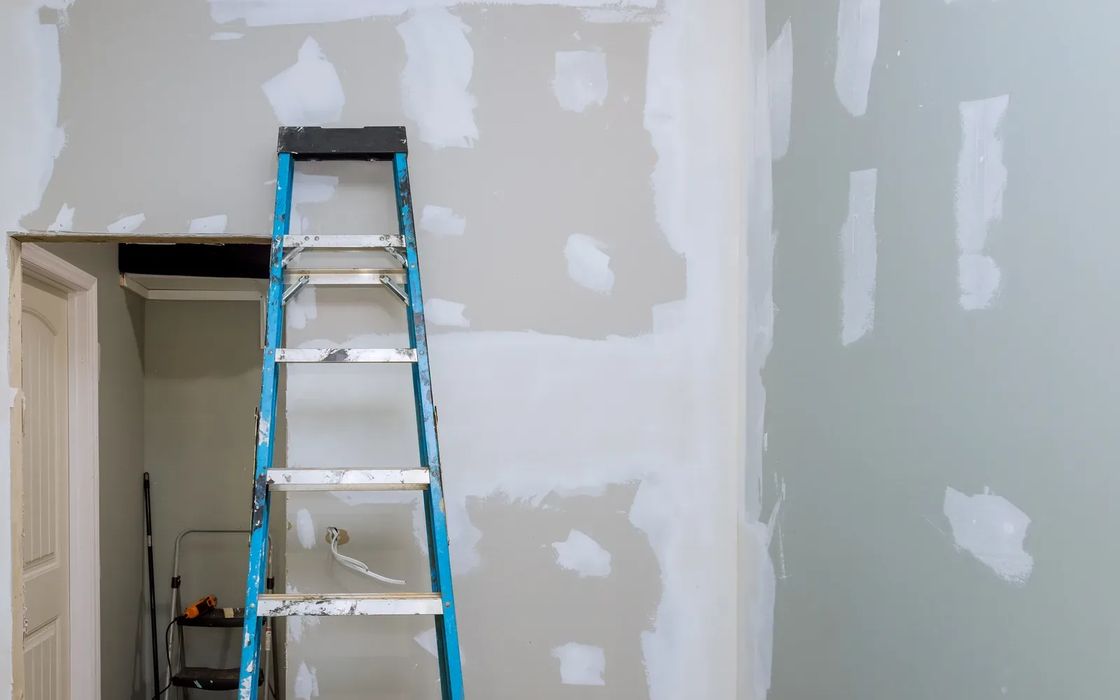 A stepladder standing in a room whose drywall is spotted with filled patches