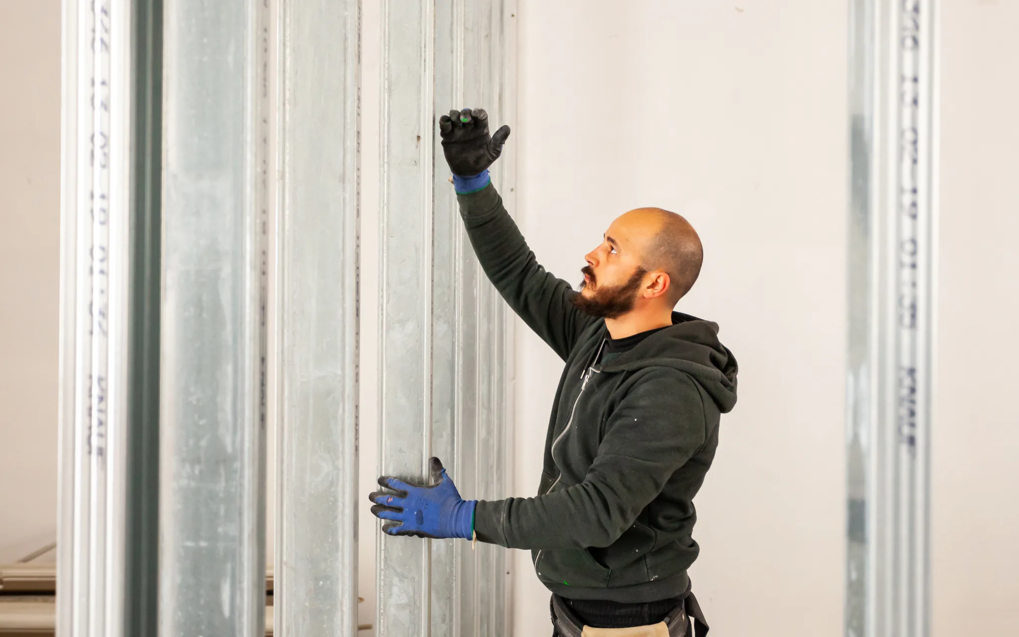 A worker setting a steel stud into its floor track during metal stud framing