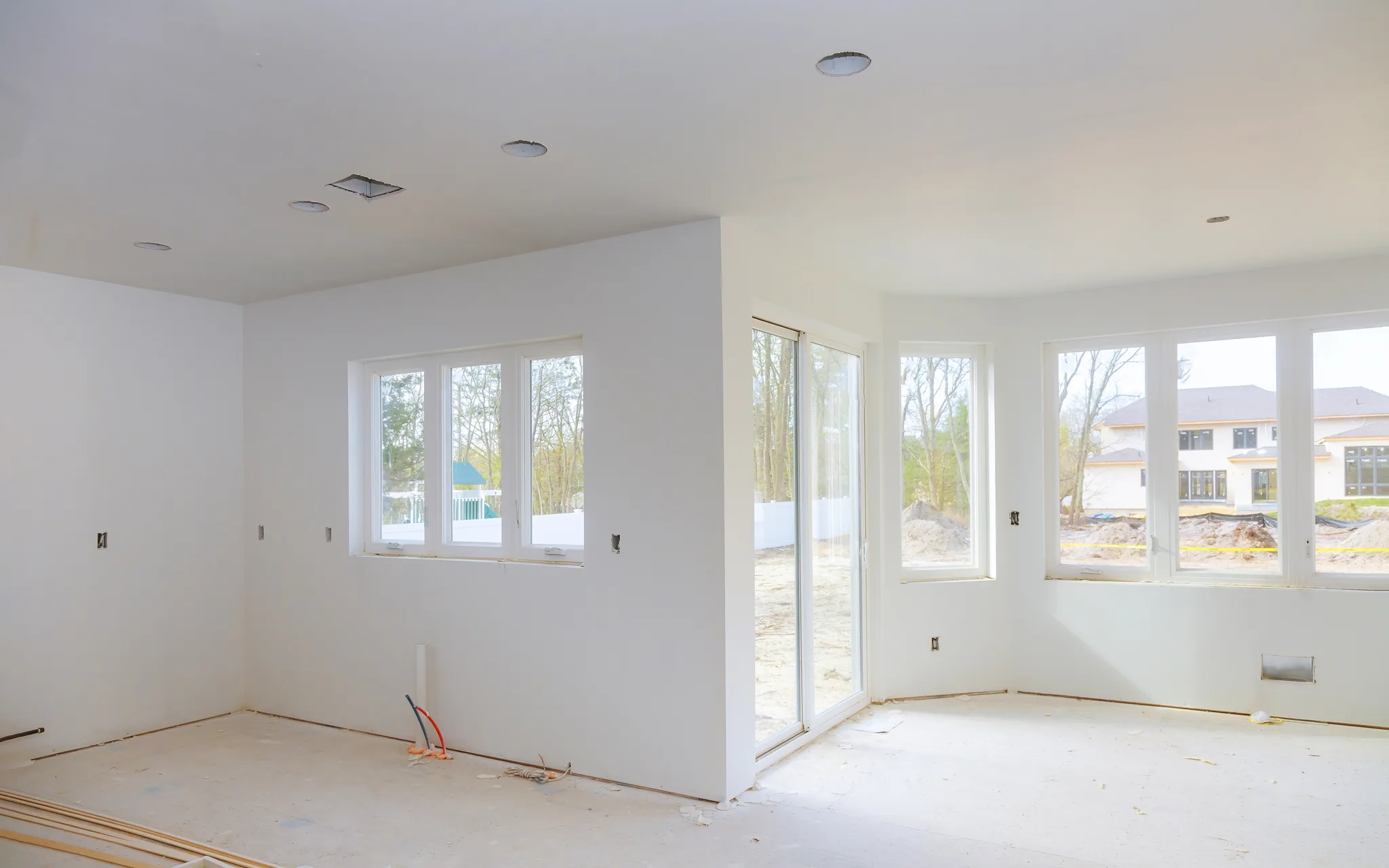 A new construction room with its drywall hung, finished and lit by three tall windows