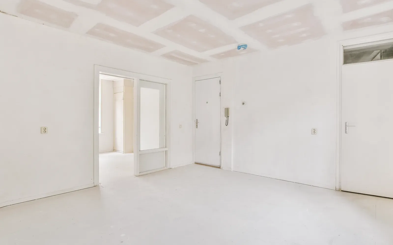 An empty room with its drywall primed and painted out, plain white walls and ceiling and no trim yet
