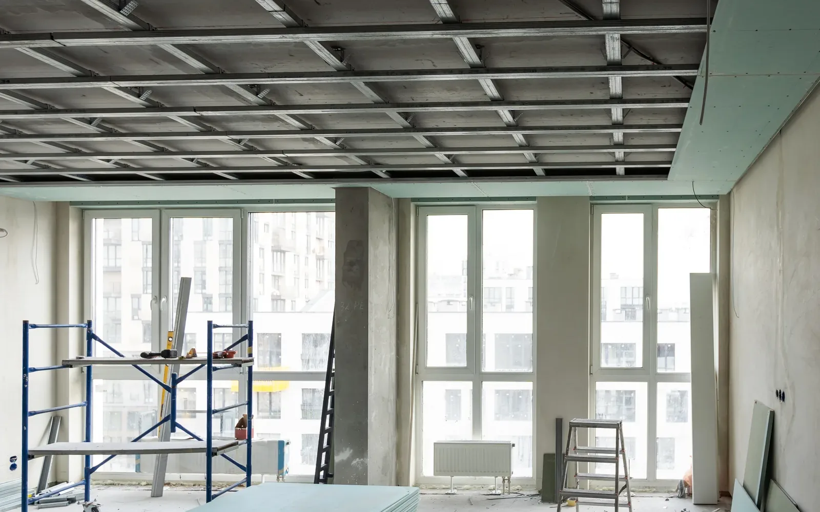 Commercial drywall work under an open suspended ceiling grid, a scaffold tower standing in the room