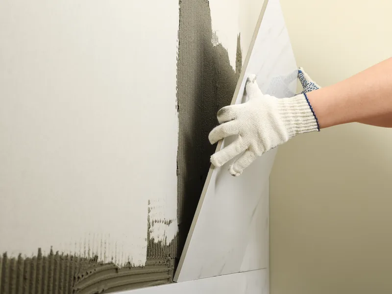 Gloved hands pressing a drywall panel onto a combed bed of adhesive