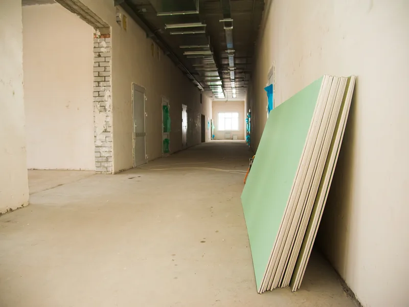 A bare institutional corridor with a green moisture-resistant panel leaning against the wall