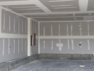 A wide commercial room boarded out in drywall with the ceiling and walls all taped