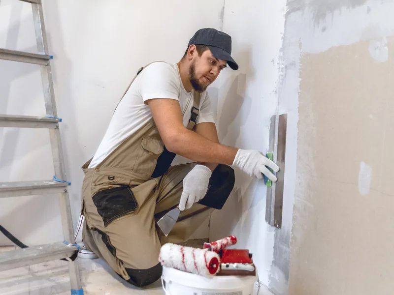 A worker crouching to fill a drywall patch low down on a wall
