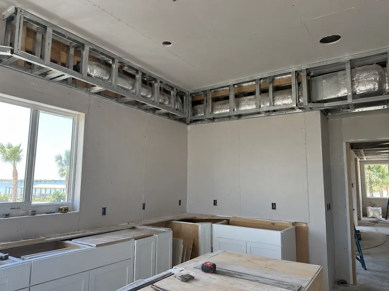 A soffit box framed in light metal along the top of a kitchen wall and around the corner, ductwork running through it