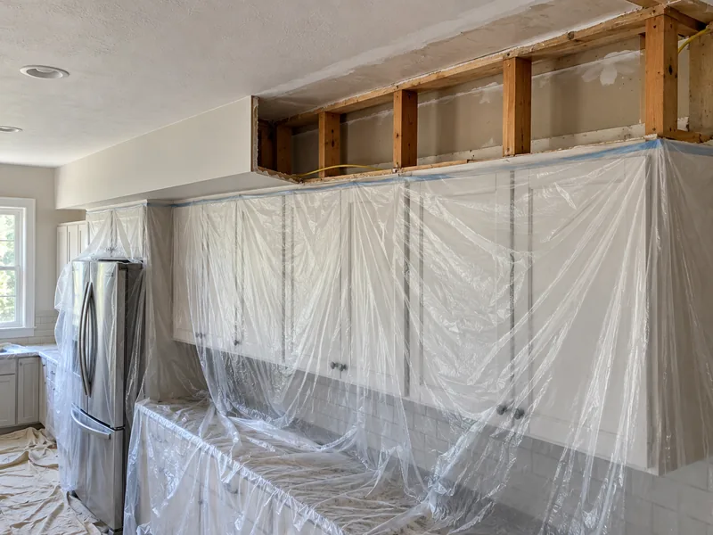 A kitchen soffit half torn out to its framing with the units sheeted over