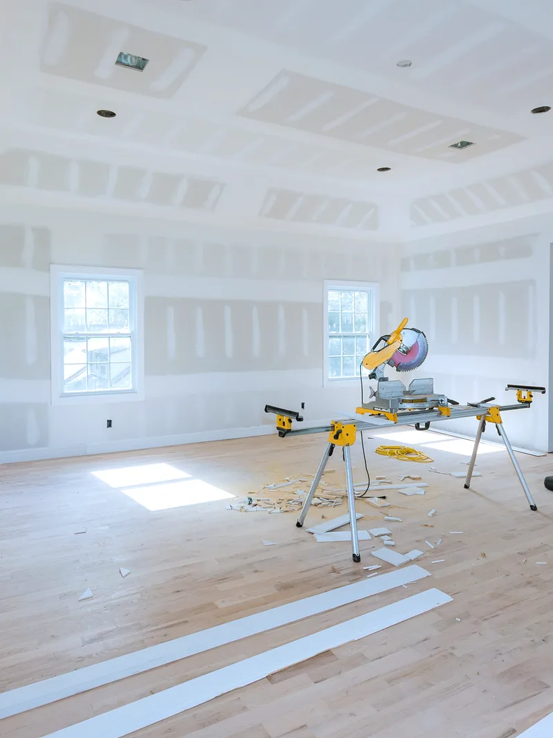 A large boarded room with a coffered ceiling and a mitre saw set up in it, architectural detail built in board