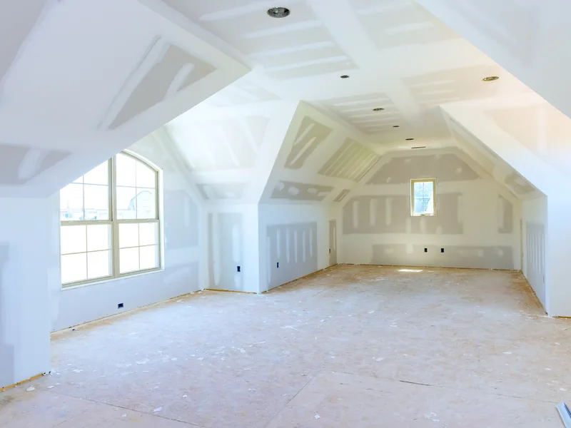 An attic room boarded out in drywall with sloping ceilings and new windows